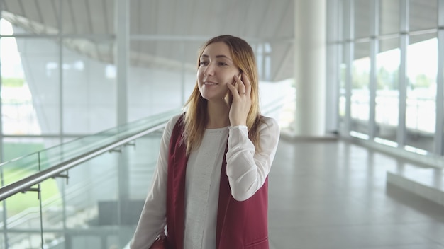 La giovane donna positiva in vestiti eleganti parla sullo smartphone mentre si imbarca sull'aereo all'aeroporto