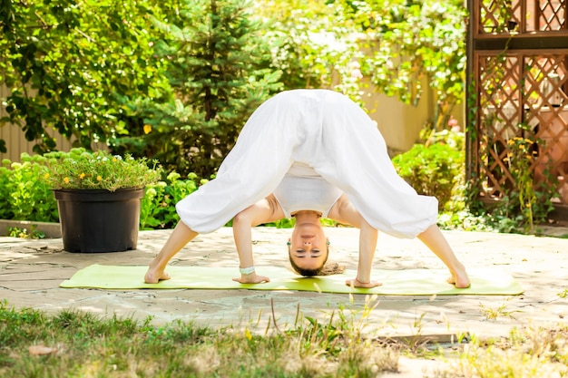 La giovane donna pratica lo yoga nel giardino Prasarita Padottanasana o piegamento in avanti della posizione larga