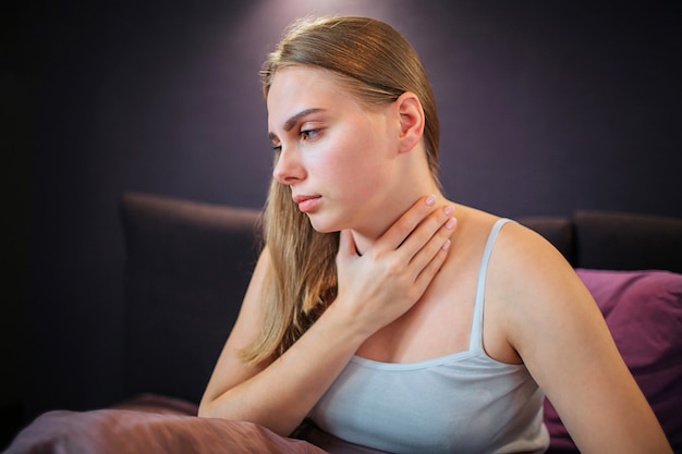 La giovane donna preoccupata si siede sul letto da solo e guarda in basso