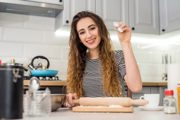 La giovane donna prepara il cibo delizioso impasta la farina sul tavolo della cucina. Cucinare cibi con ingredienti diversi