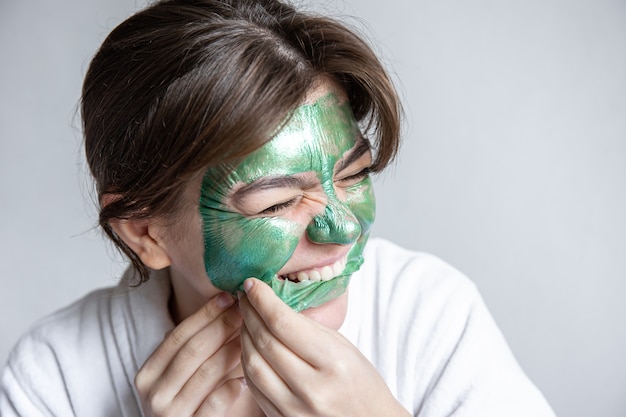 La giovane donna rimuove la maschera verde dal viso, maschera al collagene per la pelle del viso, procedura spa.