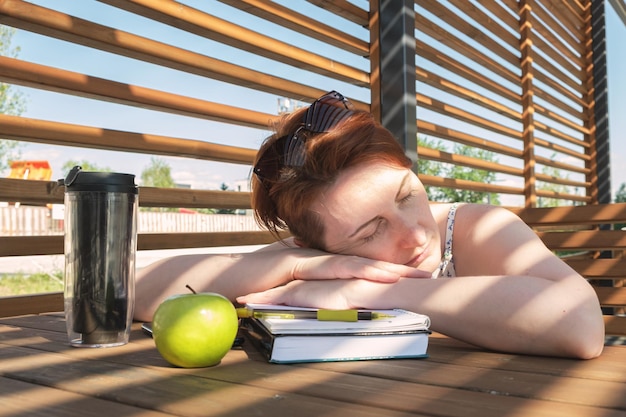 La giovane donna rossa si è addormentata sul tavolo sulla terrazza estiva mentre studiava