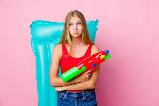 La giovane donna russa che gioca con una pistola ad acqua con un materasso ad aria soffia sulle guance, ha un'espressione stanca. Concetto di espressione facciale.