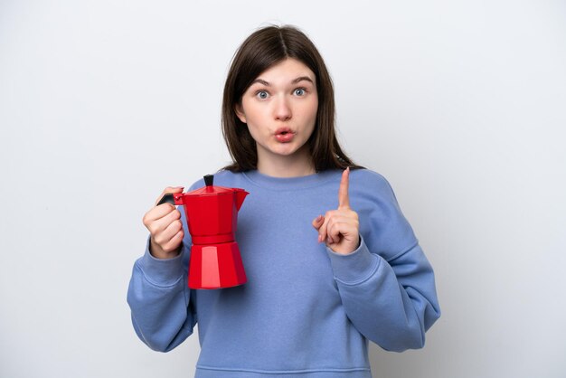La giovane donna russa che tiene la caffettiera isolata su sfondo bianco con l'intenzione di realizzare la soluzione sollevando un dito