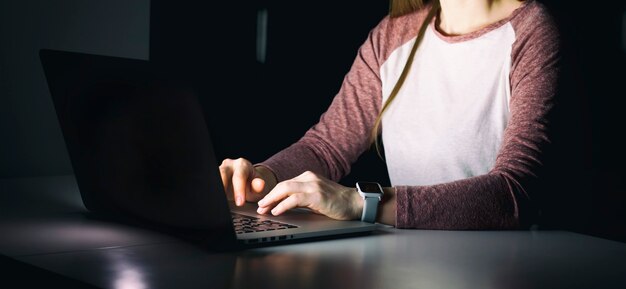 La giovane donna seduta nel soggiorno buio e che lavora con il laptop