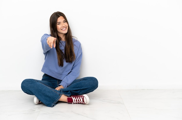 La giovane donna seduta sul pavimento ti punta il dito contro con un'espressione sicura