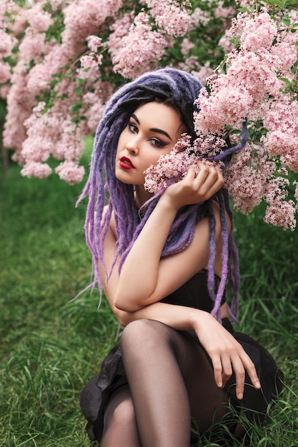 la giovane donna sexy con i dreadlocks di colore è seduta sotto l'albero in fiore