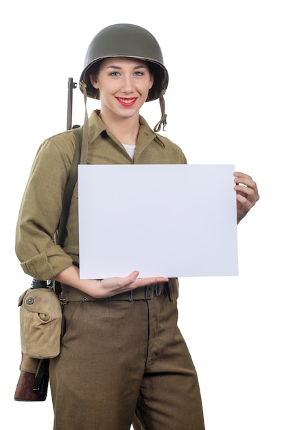 La giovane donna si è vestita nell&#39;uniforme militare di wwii con il casco che mostra l&#39;insegna in bianco vuota