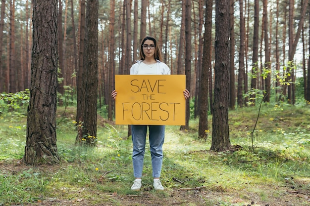 La giovane donna si offre volontaria nei picchetti dei boschi e tiene in mano un poster per salvare la foresta