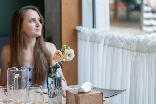 La giovane donna si siede al tavolo nella caffetteria e guarda fuori dalla finestra Ristorante accogliente La ragazza sta aspettando il suo ordine nel ristorante