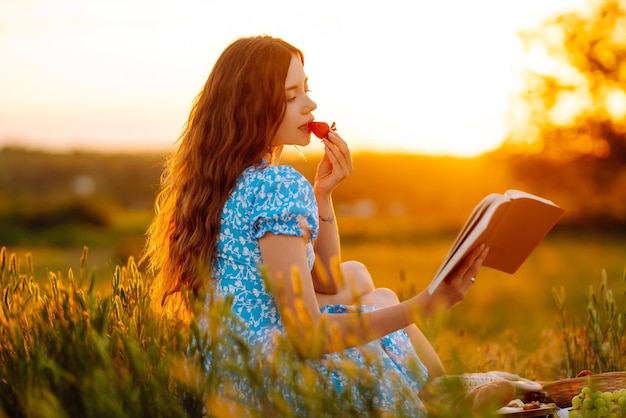 La giovane donna si siede su un plaid con un libro Picnic estivo nella natura Cibo sano