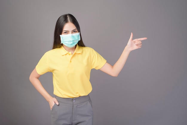 La giovane donna sicura in camicia gialla sta indossando la maschera chirurgica sopra grey