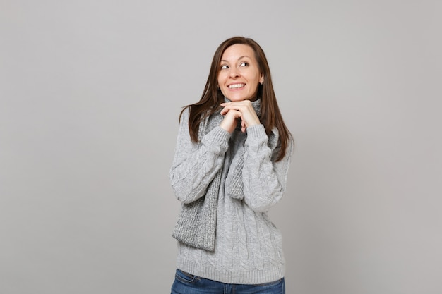 La giovane donna sognatrice in maglione grigio, sciarpa ha messo la mano sul mento isolato su sfondo grigio in studio. Stile di vita sano, persone sincere emozioni, concetto di stagione fredda. Mock up copia spazio.