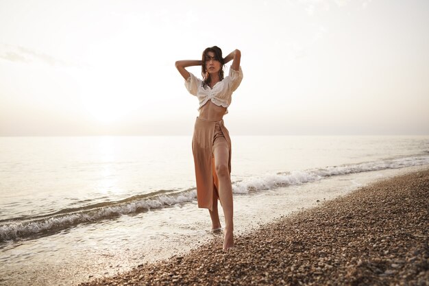 La giovane donna sola cammina sulla riva del mare al tramonto