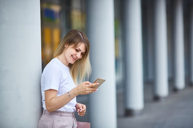 La giovane donna sorride e tiene nelle sue mani e guarda lo smartphone. Copia spazio.