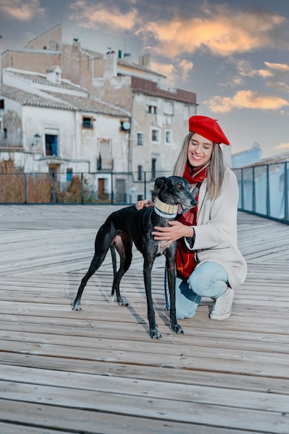 La giovane donna sorridente accarezza il suo cane durante il tramonto.