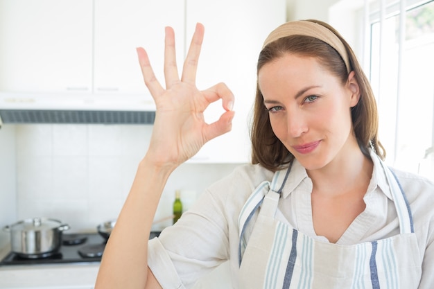 La giovane donna sorridente che gesturing l&#39;approvazione firma dentro la cucina