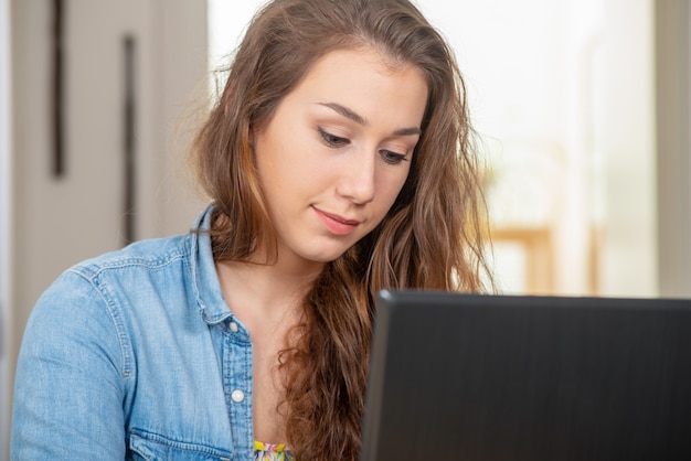 La giovane donna sorridente con capelli lunghi sta utilizzando un computer portatile