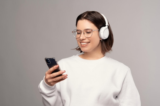 La giovane donna sorridente sta guardando il telefono mentre indossa i telefoni auricolari