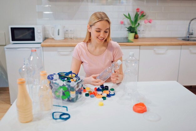 La giovane donna sorridente sta ordinando la bottiglia e i coperchi di plastica vuoti mentre si sedeva al tavolo