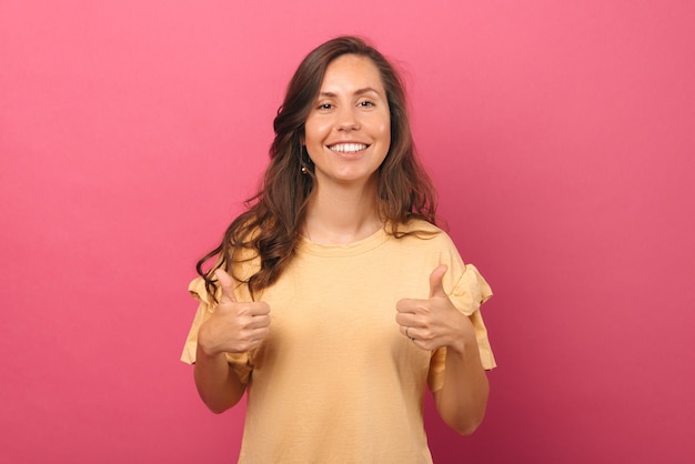 La giovane donna sorridente sta tenendo due pollici in su per un simile o una raccomandazione