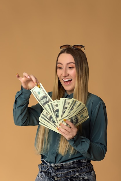 La giovane donna sorridente tiene il denaro contante in banconote in dollari