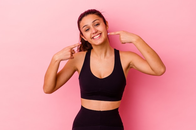 La giovane donna sportiva isolata sul muro rosa sorride, puntando le dita alla bocca