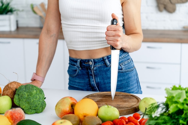 La giovane donna sportiva sta tagliando l'arancia fresca per il succo di frutta in cucina.