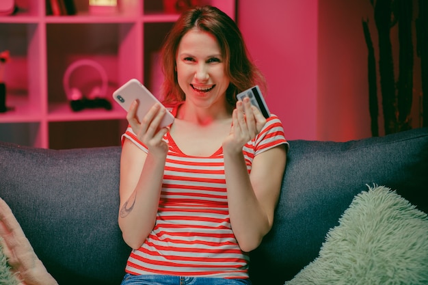 La giovane donna sta acquistando online con una carta di credito mentre era seduto sul divano in salotto.