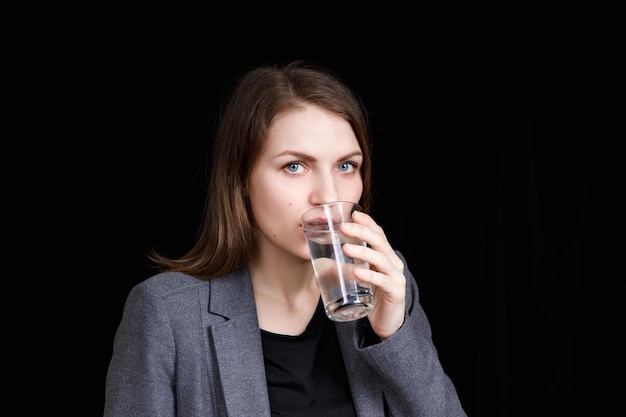 La giovane donna sta bevendo acqua pulita pura dal vetro