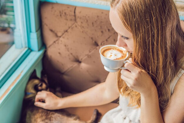 La giovane donna sta bevendo il caffè e accarezzando il gatto.