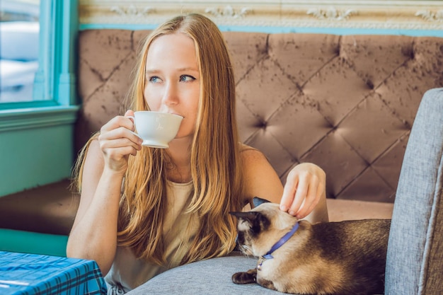 La giovane donna sta bevendo il caffè e accarezzando il gatto.
