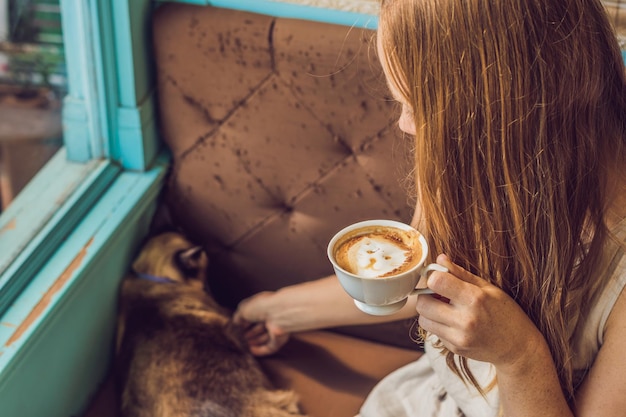 La giovane donna sta bevendo il caffè e accarezzando il gatto.