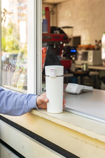 La giovane donna sta comprando il caffè in un bar con in mano la sua tazza riutilizzabile