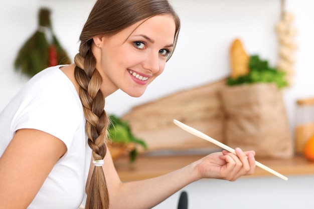 La giovane donna sta cucinando in una cucina La casalinga sta gustando la zuppa con un cucchiaio di legno