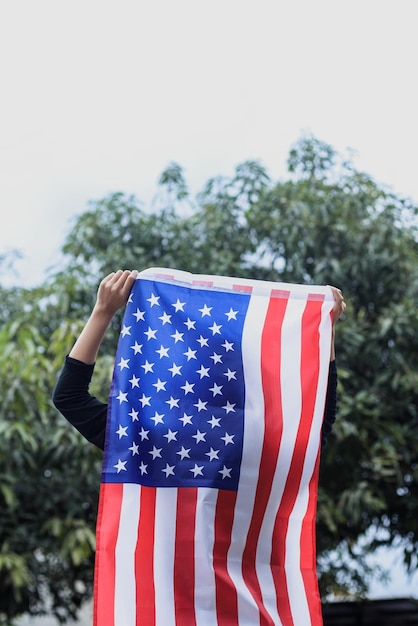 La giovane donna sta e tiene una bandiera americana all'aperto