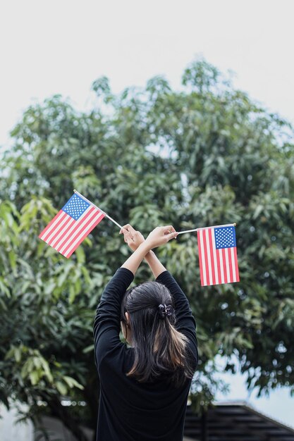 La giovane donna sta e tiene una bandiera americana all'aperto