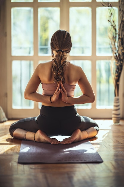 La giovane donna sta facendo yoga indietro namaste posa durante la pandemia di coronavirus nel soggiorno di casa. Sta meditando sul tappetino al sole del mattino.