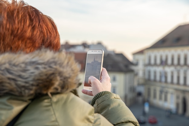 La giovane donna sta guardando Brno da una terrazza panoramica. Scatta foto della città al telefono e condividila sul sito social