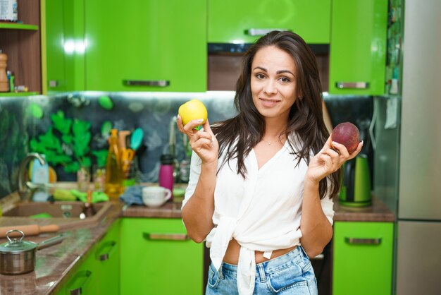 La giovane donna sta in cucina tenendo la frutta nelle sue mani