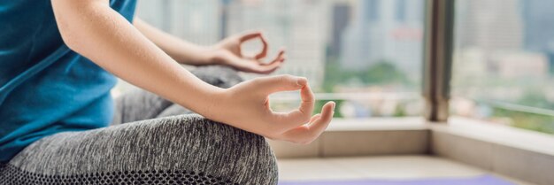 La giovane donna sta praticando lo yoga al mattino sul suo balcone con una vista panoramica della città e dei grattacieli BANNER formato lungo