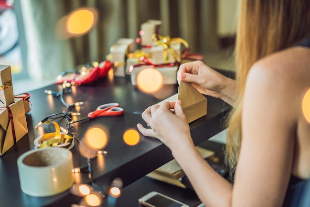 La giovane donna sta preparando i regali avvolti in carta artigianale con un nastro rosso e oro per