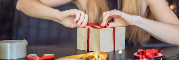 La giovane donna sta preparando i regali avvolti in carta artigianale con un nastro rosso e oro per