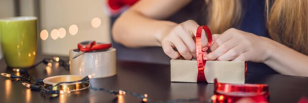 La giovane donna sta preparando i regali avvolti in carta artigianale con un nastro rosso e oro per