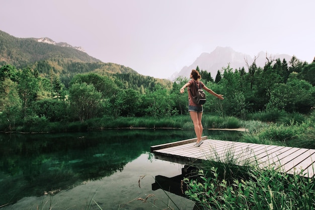 La giovane donna sta su un ponte di legno con le braccia alzate sullo sfondo della natura