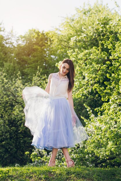 La giovane donna sta su una collina sullo sfondo di alberi in fiore