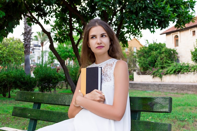 La giovane donna sta tenendo un libro e sta sognando di qualcosa all&#39;esterno