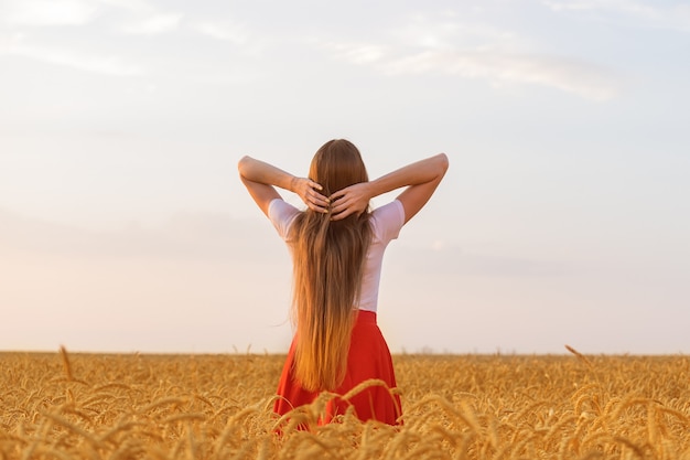 La giovane donna sta tra i campi di grano. Retrovisore. Bei capelli lunghi. Bellezza naturale.