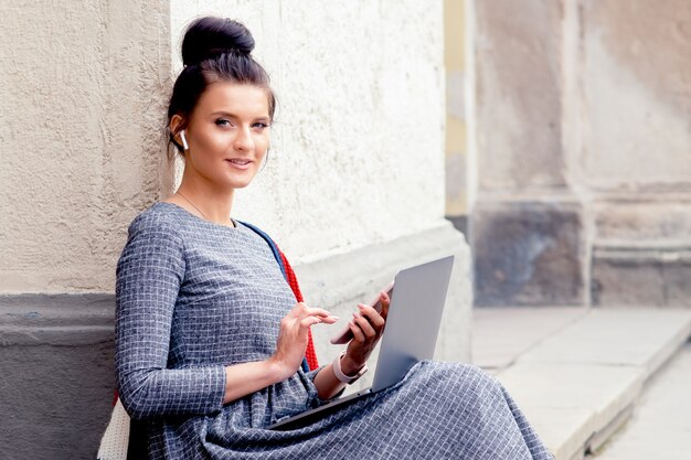 La giovane donna sta usando il telefono e il computer portatile all'aperto