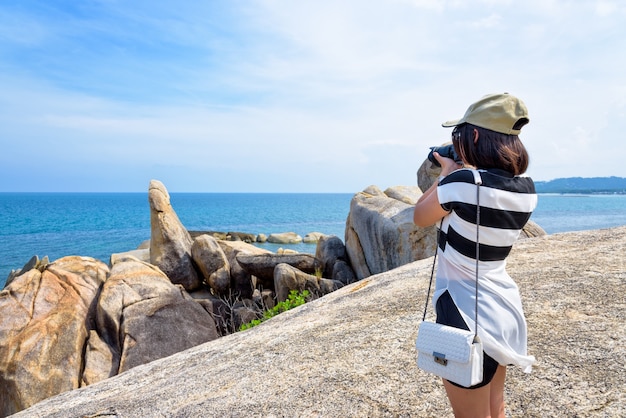 La giovane donna sta usando una fotocamera DSLR per fotografare l'Hin Ta Hin Yai e il bellissimo paesaggio naturale del mare e del cielo blu durante il viaggio estivo all'isola di Koh Samui, Surat Thani, Thailan